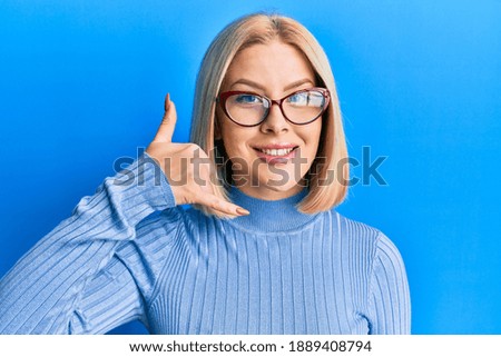 Young blonde woman wearing casual clothes and glasses smiling doing phone gesture with hand and fingers like talking on the telephone. communicating concepts. 