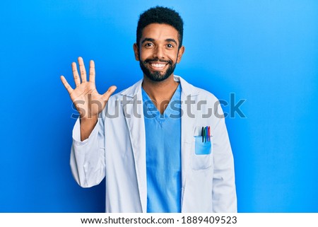 Handsome hispanic man with beard wearing doctor uniform showing and pointing up with fingers number five while smiling confident and happy. 