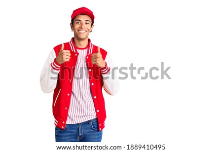 Young african amercian man wearing baseball uniform success sign doing positive gesture with hand, thumbs up smiling and happy. cheerful expression and winner gesture. 