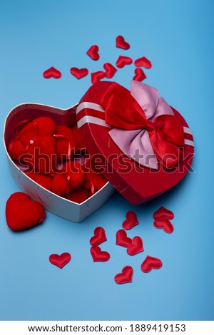 Heart shaped gift box filled with hearts on a blue background. Happy Valentines Day. Vertical picture