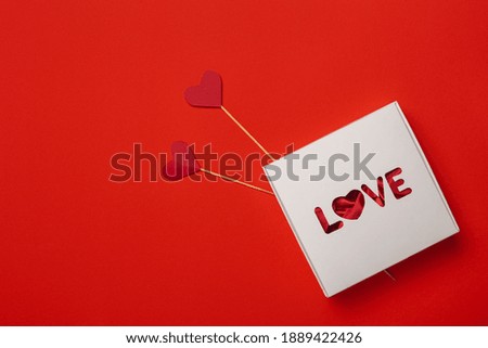 Gift box with the text Love and hearts on a stick on a red background. Composition Valentine's Day. Banner. Flat lay, top view.