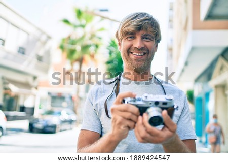 Young irish photographer man smiling happy using vintage camera at street of city.
