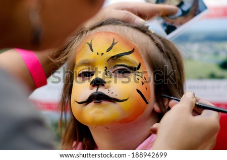 Young girl (female age 4-5) getting her face painted like a lion by a face painting make up artist on Halloween or Purim carnival Jewish holiday. Real people. Copy space Royalty-Free Stock Photo #188942699