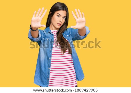 Young brunette woman wearing casual clothes doing frame using hands palms and fingers, camera perspective 