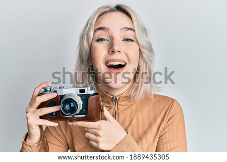 Young blonde girl holding vintage camera smiling and laughing hard out loud because funny crazy joke. 