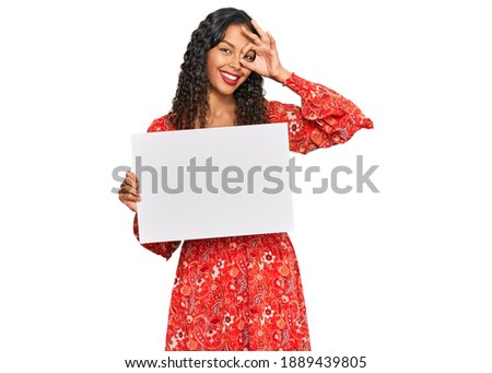 Young african american girl holding blank empty banner smiling happy doing ok sign with hand on eye looking through fingers 
