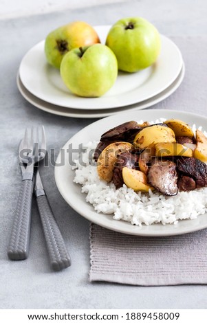 Fried chicken liver with apples served with white rice on a plate. Green apples on background