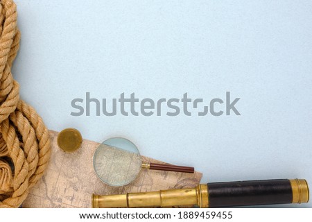 Top view of vintage spyglass, magnifier, map and nautical rope. On a blue background.