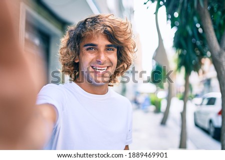 Young handsome hispanic man smiling happy making selfie by the camera at street of city