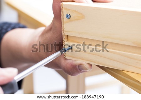 A carpenter builds a small white table with a screwdriver Royalty-Free Stock Photo #188947190