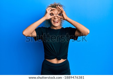 Beautiful caucasian teenager girl wearing black sportswear doing ok gesture like binoculars sticking tongue out, eyes looking through fingers. crazy expression. 
