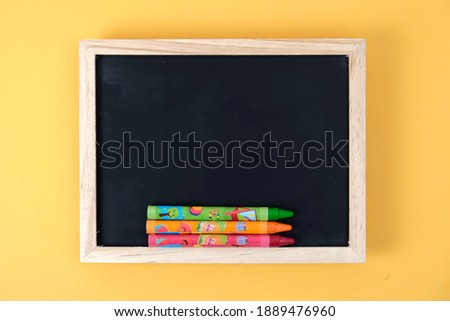 colorful crayon and wood black board on yellow background 