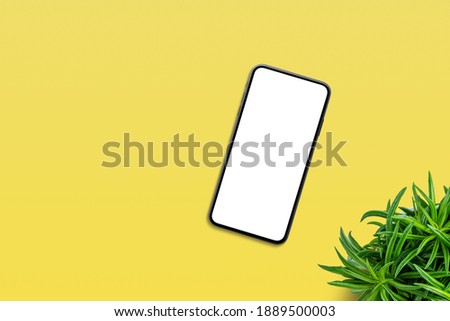 Phone on yellow table with plant beside. Top view, flat lay composition with copy space. Isolated screen for app or web site design promotion