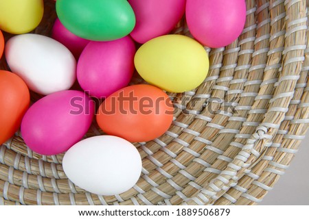 Brightly colored easter eggs, in a straw basket against a grey background.