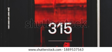 White house number on a red glass inserted in a black wooden door, reflection, Montreal, Canada