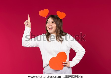 Happy girl with red hearts raised her index finger to the top. An idea with space for your advertisement. High quality photo
