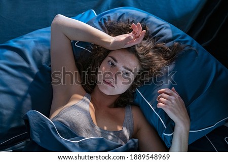Stressed woman on bed late at night suffering from insomnia, sleep apnea or stress. Top view of depressed girl lying in bed late at night. High angle view of awake girl in the middle of the night. Royalty-Free Stock Photo #1889548969