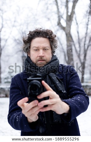 Caucasian man in the middle of the snow taking a picture watching the screen of his camera