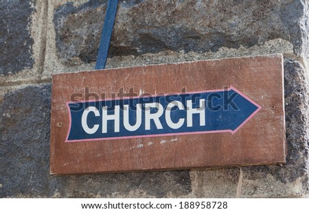 old brown wood church sign with blue arrow on dark stone wall