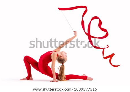 Girl gymnast in a red overalls does exercise with a ribbon on a white background, the ribbon curled into a heart, isolate