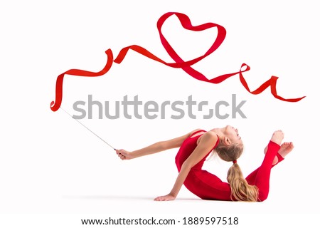 Isolated on white background Girl gymnast in a red overalls does exercise with a ribbon, the ribbon is twisted into a heart.