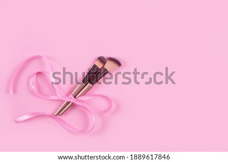 Professional cosmetic makeup brush bounded with pink ribbon bow on light pink background with copy space for your text. Creative make-up concept, selective focus