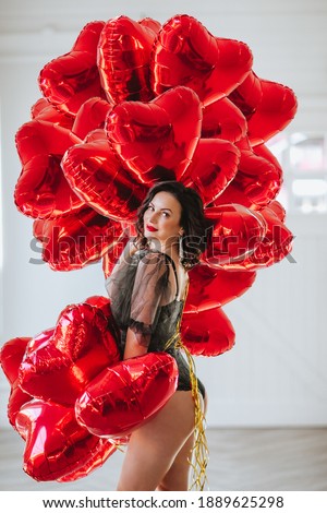 Pretty brunette woman in black body posing with bunch of red balloons like a hearts against white background.
