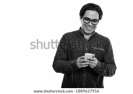 Studio shot of young happy Persian man smiling while using mobile phone