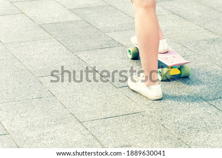 Close up of feet of a girl in white sneakers and pink penny skate board. Outdoor lifestyle picture on a sunny summer day.