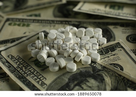 Lots of pills on the background of lots of hundred dollar bills