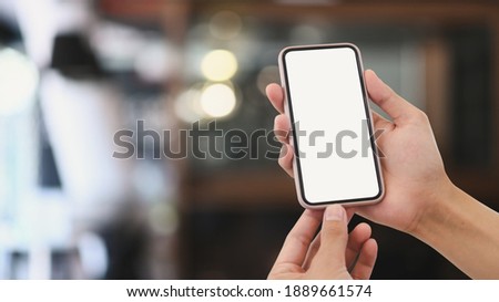 Close up view of man hands holding mock up smart phone with modern cafe blurred background.