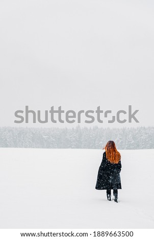young teenage girl with long hair in black coat walking on show field. Winter outdoor photo