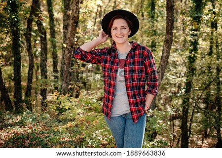 traveler hipster woman standing alone in black hat and checkered shirt in autumn woods . Cold weather, fall colors. Wanderlust concept.