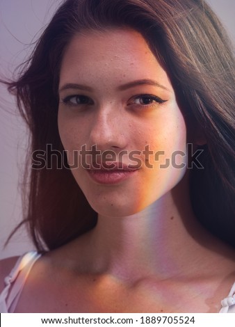 portrait of one young woman, posing in photo studio with white background and rainbow light effect created from prism.