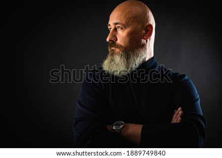 close up photo, portrait of a serious, thoughtful, bearded man on a dark background confident and dramatic looking straight. Concept of male portrait.  Low key 