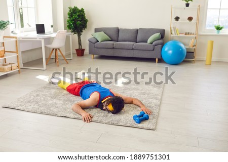 Tired exhausted young sportsman decided to take a break after failing to do push-ups during sports workout at home. Funny male athlete is lying on floor after giving up fitness training with dumbbells Royalty-Free Stock Photo #1889751301