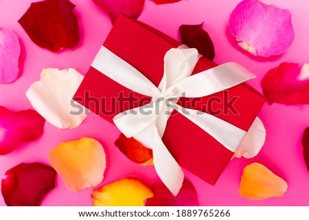 pink bright background with colored rose petals and a red gift box with a bow in the center valentines day discounts promotion