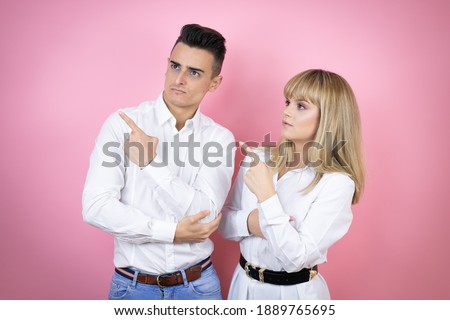 Young couple of girlfriend and boyfriend over isolated pink background confused and pointing with hand and finger to the side