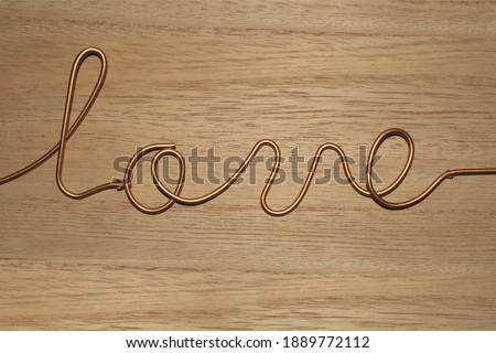 Word love made out of gold or copper wire on wooden background . Close-up . Decoration
