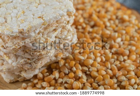 Stack of tasty crispbread and raw corns on blurry background