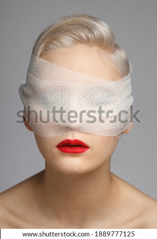 young woman wearing white blindfold isolated on grey background