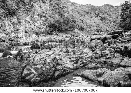 A black and white photo of a scenic rocky river flowing through a deep, remote mountain valley in Japan.