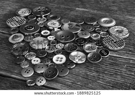 A black and white top view image of old vintage buttons in a heart shape on an dark wooden table. 