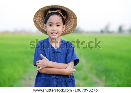 Asian boy wear farmer shirt and hat smile at a green rice farm
