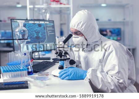 Healthcare researcher analying sample on microscope dressed in ppe suit. Virolog in coverall during coronavirus outbreak conducting healthcare scientific analysis. Royalty-Free Stock Photo #1889919178