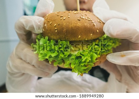 Man in rubber gloves holding a burger.