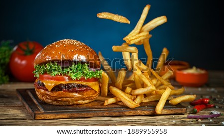 French fries fall next to cheeseburger, lying on vintage wooden cutting board, Freeze motion. Royalty-Free Stock Photo #1889955958
