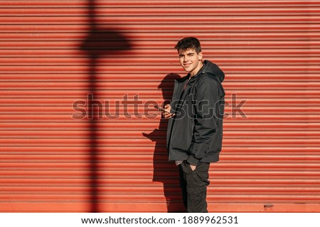 teenager on the street with mobile phone in front of red blind