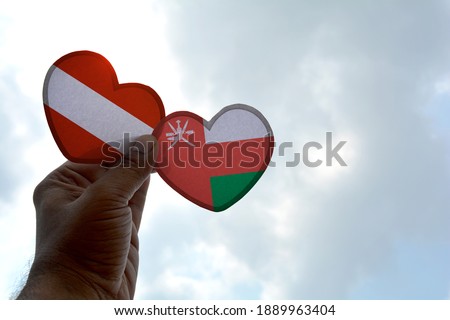 Hand holds a heart Shape Austria and Oman flag, love between two countries