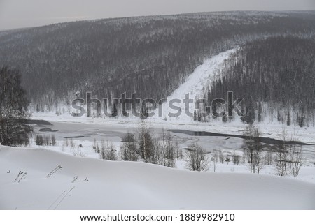 Valley of the frozen river with snow-capped banks and wooded hills in winter